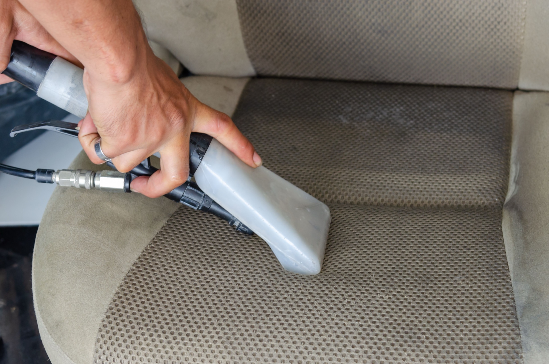A fabric vehicle seat being cleaned with an extraction tool